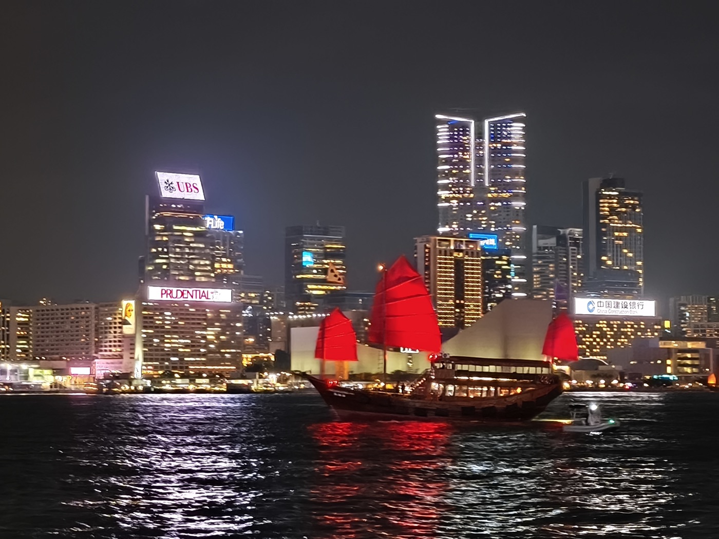 A junk boat with red sails on Victoria Harbour at night