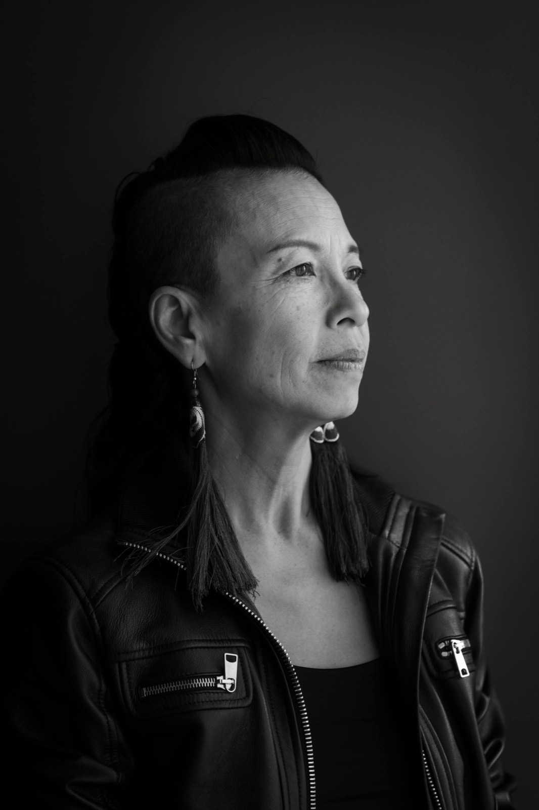 Black and white profile portrait of Angel Cheng in a leather jacket with long tassel earrings