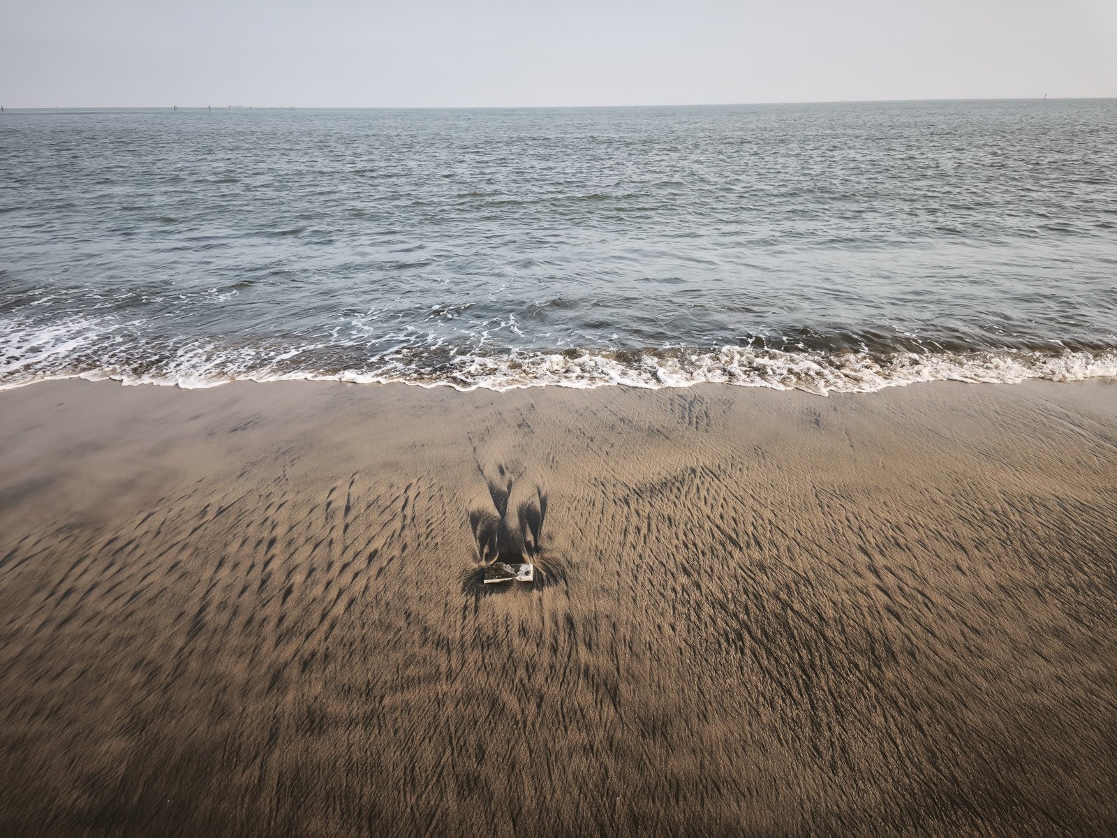 A blurred figure crouching on wet sand at the edge of a grey sea
